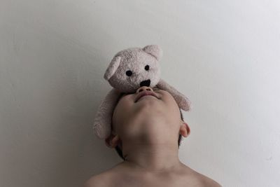 Teddy bear on boy face against wall at home