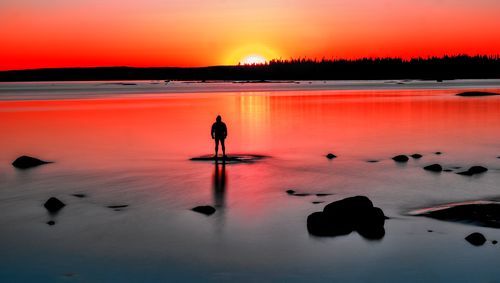 Rear view of man standing on lake during sunset