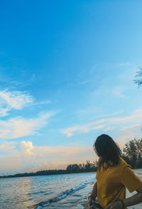 Rear view of woman standing by sea against sky