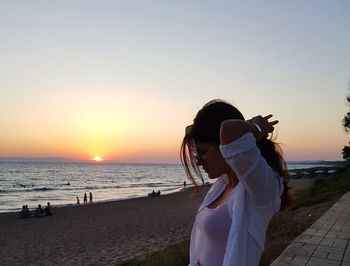 Woman standing on beach against sky during sunset