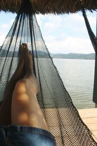Low section of woman relaxing in hammock against lake