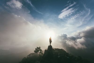 Silhouette man standing on rock against clouds