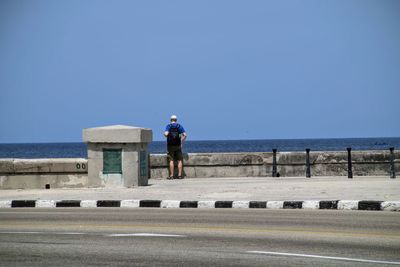 Rear view of standing by retaining wall against sea