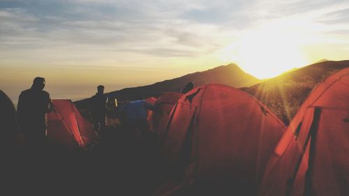 People standing by tents against sky during sunset