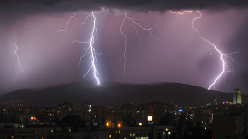 Lightning over illuminated cityscape against sky at night