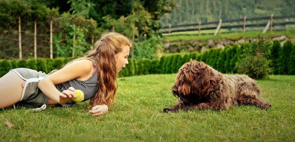 Side view of woman lying on grass while playing with pudelpointer