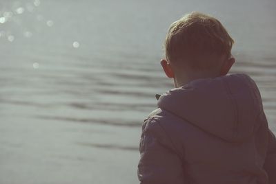 Rear view of boy by lake on sunny day