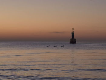 Lighthouse by sea against sky during sunset