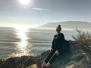 Portrait of girl leaning on rock by sea against sky