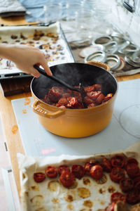 Crop unrecognizable housewife with spatula holding hot pan with cooked tomatoes while preparing delicious sauce in kitchen