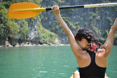 Rear view of woman holding oar while sitting on kayak in sea