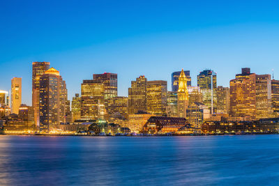 Illuminated buildings in city against clear blue sky