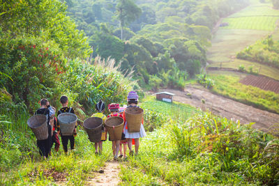Rear view of children with wicker baskets walking on field