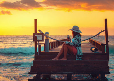 Woman sitting on beach against sky during sunset