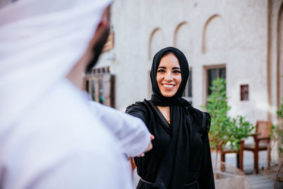 Smiling couple holding hands while standing against building