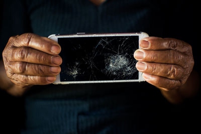 Close-up of woman holding damaged phone against black background