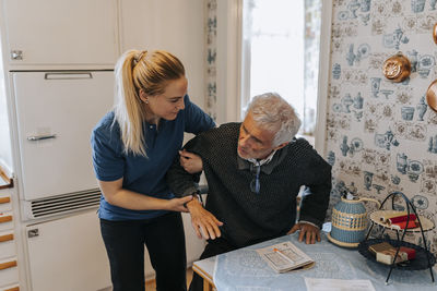 Female caregiver helping senior man in getting up at home