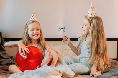 Happy children, girls, sisters, twins at home bed morning on their birthday festive caps red balloon