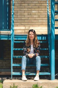 Portrait of young woman sitting against brick wall