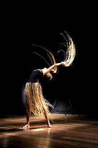 Contemporary dancer dancing in theater with black background and straw accessory. 