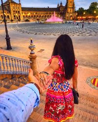 Rear view of woman holding hands of men on staircase in city