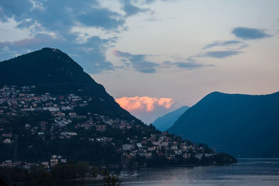 Houses on mountain by lake against sky during sunset