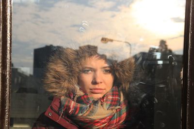 Portrait of young woman wearing warm clothing seen through window