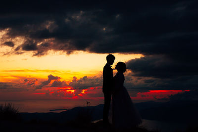 Silhouette couple standing against orange sky