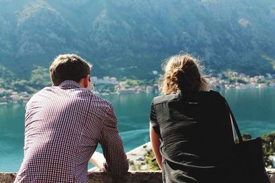 Rear view of friends sitting by lake against mountain