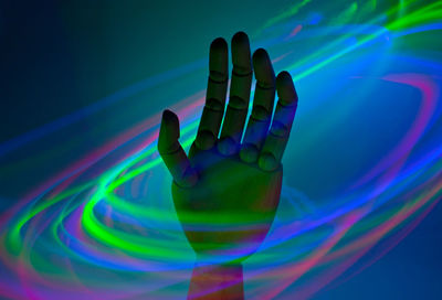 Digital composite image of hand against illuminated colored background