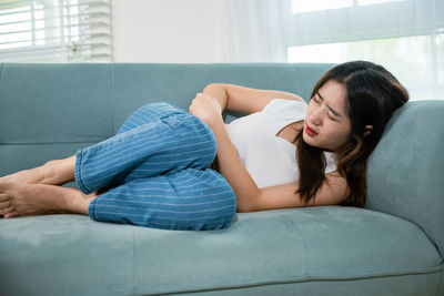 Young woman using phone while sitting on sofa at home