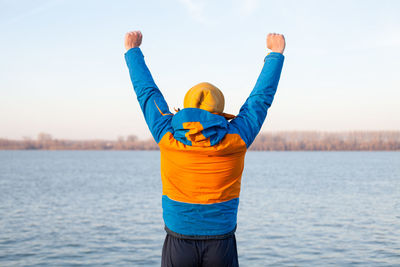 Rear view of man with arms raised standing by river