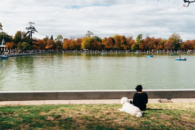 Rear view of man sitting by lake against sky