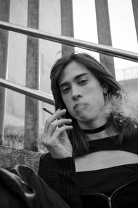 Close-up of young man holding a cigar while blowing smoke from his mouth.