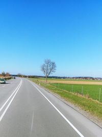 Road amidst field against clear blue sky