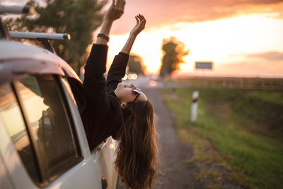 Beautiful woman leaning out from car window during sunset