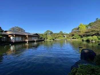 Scenic view of river by trees and buildings against clear blue sky