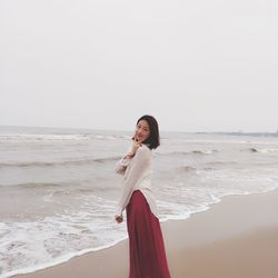 Portrait of woman gesturing peace sign while standing at beach