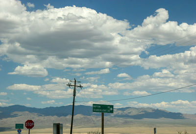 Road sign by electricity pylon against sky