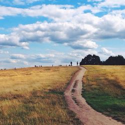 Dirt road in field against cloudy sky