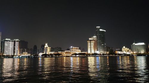 Sea by illuminated buildings against sky at night