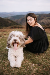 Cute fluffy spanish water dog giving paw for smiling female owner while sitting together on grassy hill in mountains