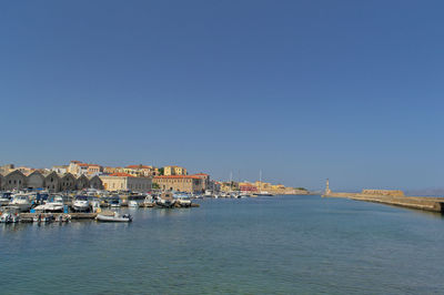 Sailboats moored on sea by buildings against clear sky