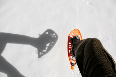 Low section of man wearing snowshoe while standing on snow covered field 