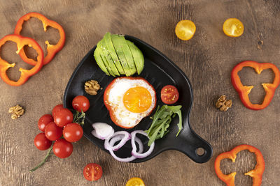 Delicious breakfast with scrambled egg, avocado, cherry tomatoes, bell peppers, and onion rings.