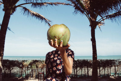 Girl holding coconut in front of face at beach