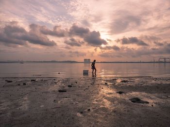 Man wading in sea against sky during sunset
