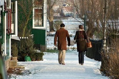 Rear view of man and woman walking on snow covered field during winter