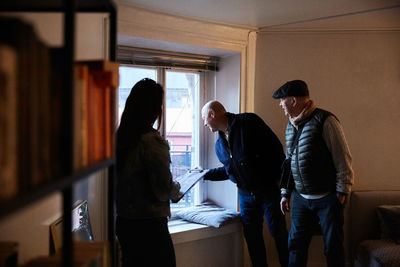 Senior men looking through window while standing with female owner at home