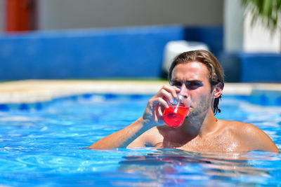 Portrait of man drinking juice in swimming pool